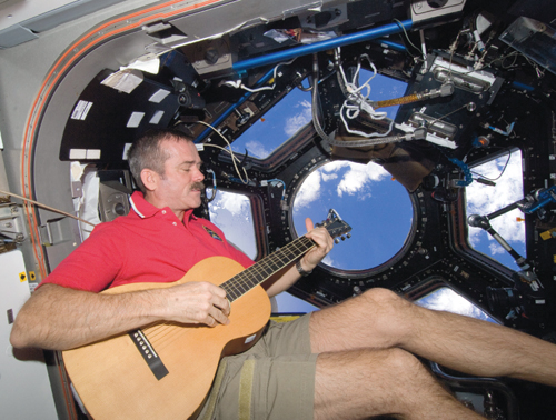 Astronaut Chris Hadfield takes a musical break in the cupola of the International Space Station, escaping from the significant amount of mechanical noise aboard the station, during Expedition 34 in 2012. <strong>Photograph courtesy of the Canadian Space Agency.</strong>