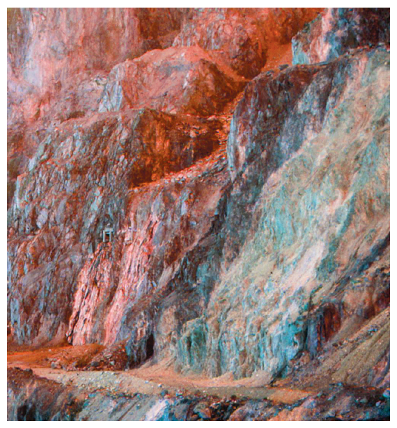 The United Verde massive pyrite deposit in Jerome, AZ, shows multicolored rocks resulting from the oxidation of pyrite. For scale, the mine entryway at center left is approximately human-sized. <strong>Image courtesy of the author and Oxford University Press.</strong>