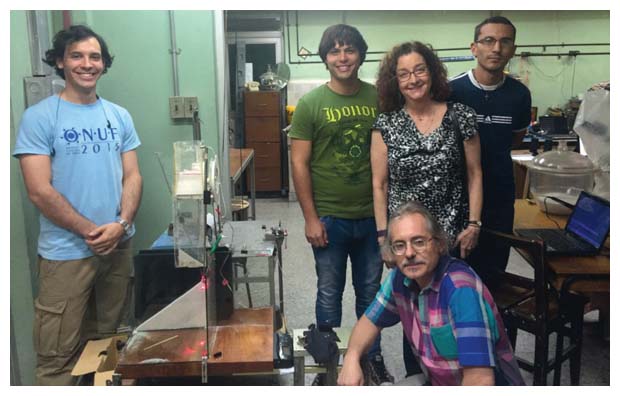 At the University of Havana, physics professor Ernesto Altshuler (<em>seated, in plaid shirt</em>) and undergraduate students show their sand-flow experiment to visitor Laura Greene, president-elect of the American Physical Society. (Standing, left to right: Leonardo Domínguez, Andy S. García, Greene, and Adrián Enrique.) <strong>Photograph by Gustavo Sánchez.</strong>